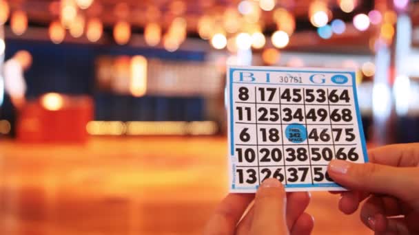 Játék kártya bingo kezében közelről homályos háttérrel, játék terem — Stock videók