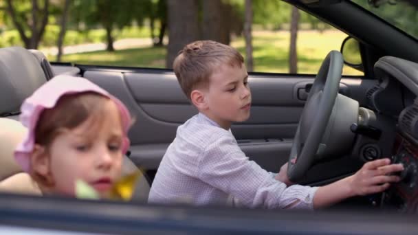 Kids sit in cabriolet, girl blows toy and brother push buttons — Stock Video