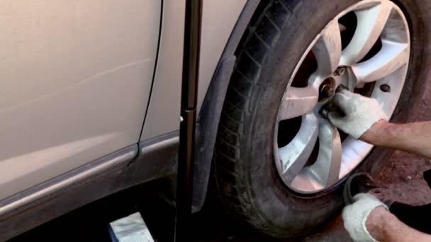 Мужчина закрутил гайки на колесе с помощью подъемного домкрата под машиной — стоковое видео