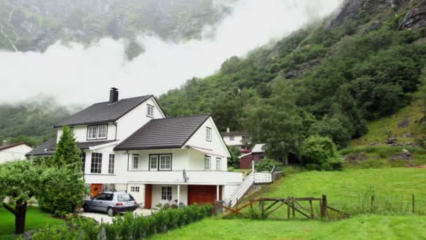 Ovejas caminan por campo cerca de casas de campo bajo la montaña — Vídeos de Stock