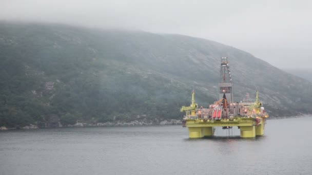 Нефтяная вышка, расположенная в море возле горы на берегу под облачным небом — стоковое видео