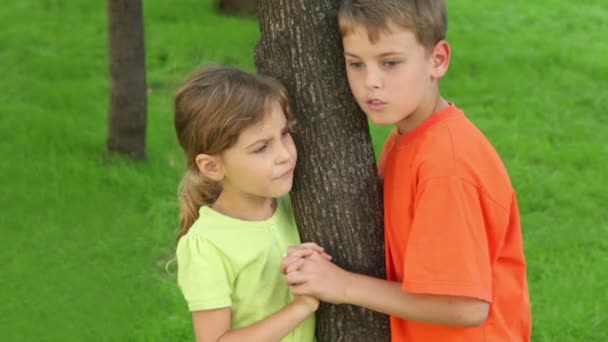 Zwei Kinder Bruder und kleine Schwester halten sich an Baum und reden — Stockvideo