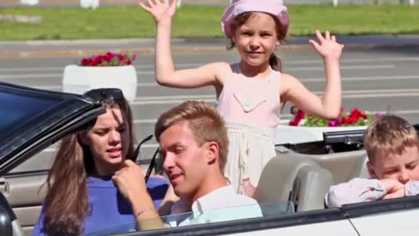 Couple sit in cabriolet, little girls wave hands at back seat — Stock Video