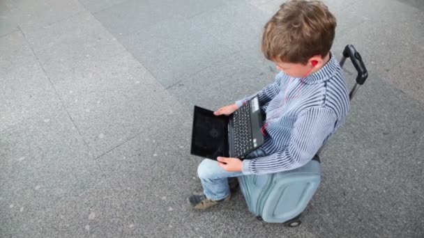 Kleiner Junge hält Netbook auf Reisetasche — Stockvideo