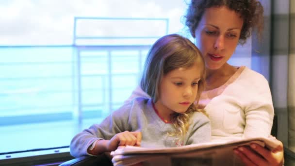 Mulher com filha senta-se na cadeira e lê jornal na cabine — Vídeo de Stock