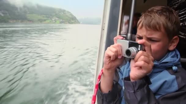 Мальчик делает фото с спасательной лодки, которая плавает на фьорде — стоковое видео