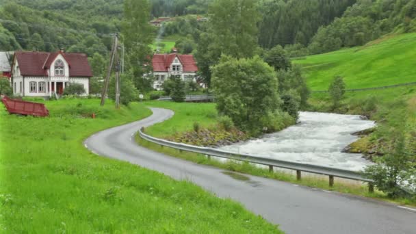 Ρεύμα του ποταμού κοντά στο δρόμο προς το χωριό ανάμεσα σε δέντρα κοντά σε βουνά — Αρχείο Βίντεο