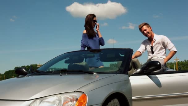 Flickan står i cabriolet med sin pojkvän sitta nära och skratta — Stockvideo