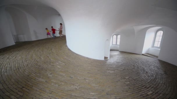 Мама з двома дітьми біжить в спіральному коридорі з мощеною підлогою — стокове відео