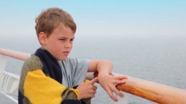 Boy wrapped in plaid stands on deck and admire seascape