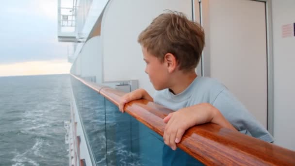 Boy looks at water, leaning on handrail of board of ship — Stock Video