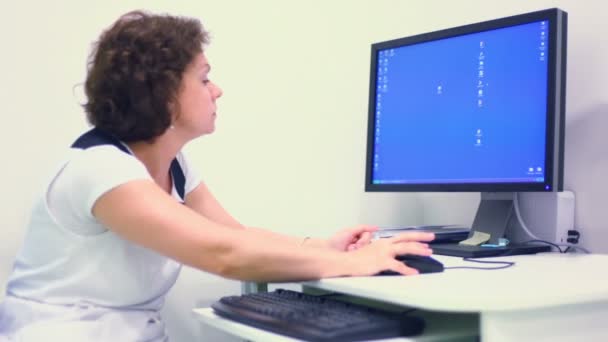 Doctor sits at work table and watches on screen of computer — Stock Video