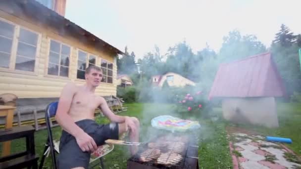 Homme assis en fumée de grill avec kebab sur la grille près de la maison — Video