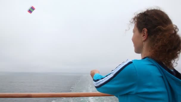 Woman by ship deck holds rope from kite in gray sky — Stock Video