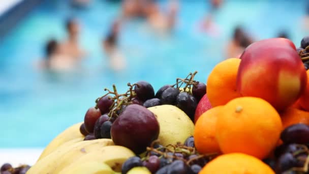 Oranges, apples, bananas, grapes close up in front of pool — Stock Video