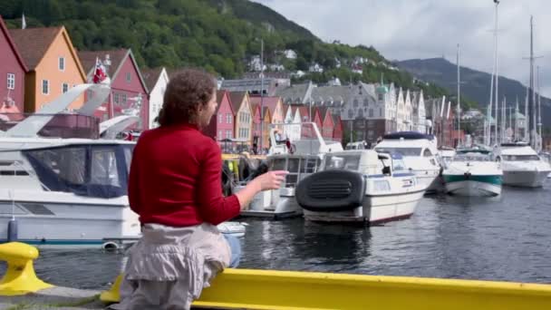 Femme assise sur le quai dans le quai avec des bateaux dans la ville côtière de Bergen — Video