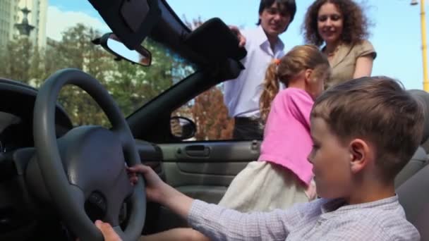 Dois meninos com menina brincam em cabriolet e os pais ficam perto — Vídeo de Stock