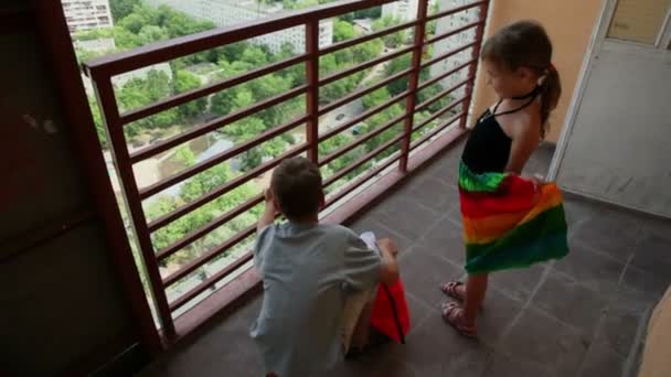 Deux enfants garçon et fille regarder sur le paysage urbain d'été depuis le balcon — Video