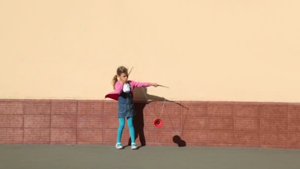 Klein meisje houdt twee stokken en speelt speelgoed in de buurt van muur — Stockvideo