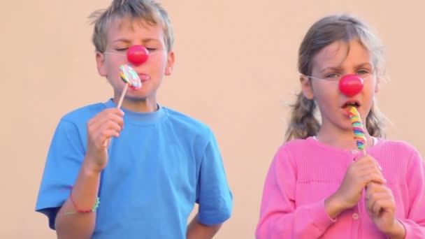 Duas crianças com narizes de palhaço comem doces coloridos — Vídeo de Stock