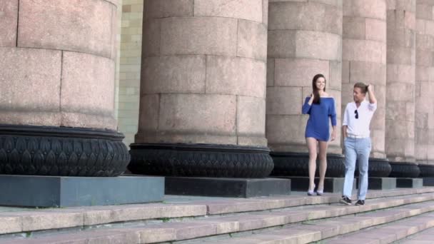 Chica en vestido azul camina con novio cerca de columnata — Vídeos de Stock
