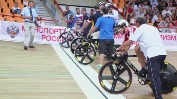 Cuatro ciclistas comienzan a montar con la ayuda de asistentes en el estadio — Vídeos de Stock