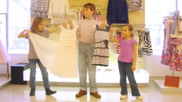 Мальчик помогает выбрать платье девочкам в магазине, время уходит — стоковое видео