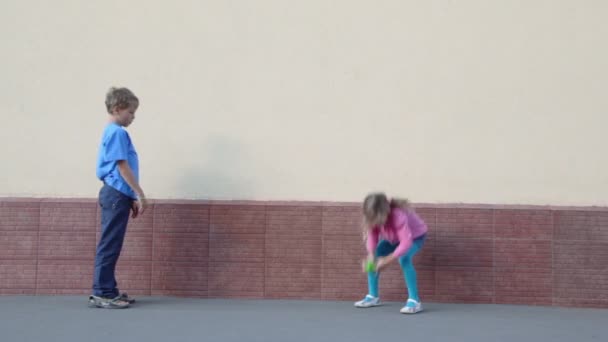 Twee kinderen jongen en meisje gooit bal met elkaar in de buurt van muur — Stockvideo