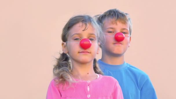 Двое детей мальчик и девочка с клоунскими носами улыбаются и моргают — стоковое видео