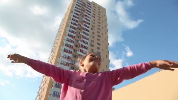 Kleine Mädchen drehen sich in der Nähe von Wohnhaus mit Armen nach oben — Stockvideo