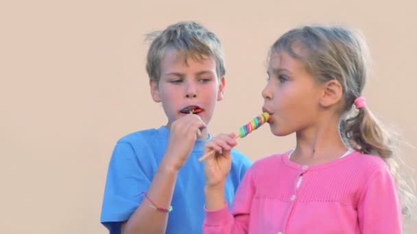 Dwoje dzieci chłopiec i dziewczynka jeść cukierki kolorowe i mówić — Wideo stockowe