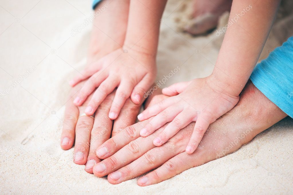 Father and daughter hands on sand