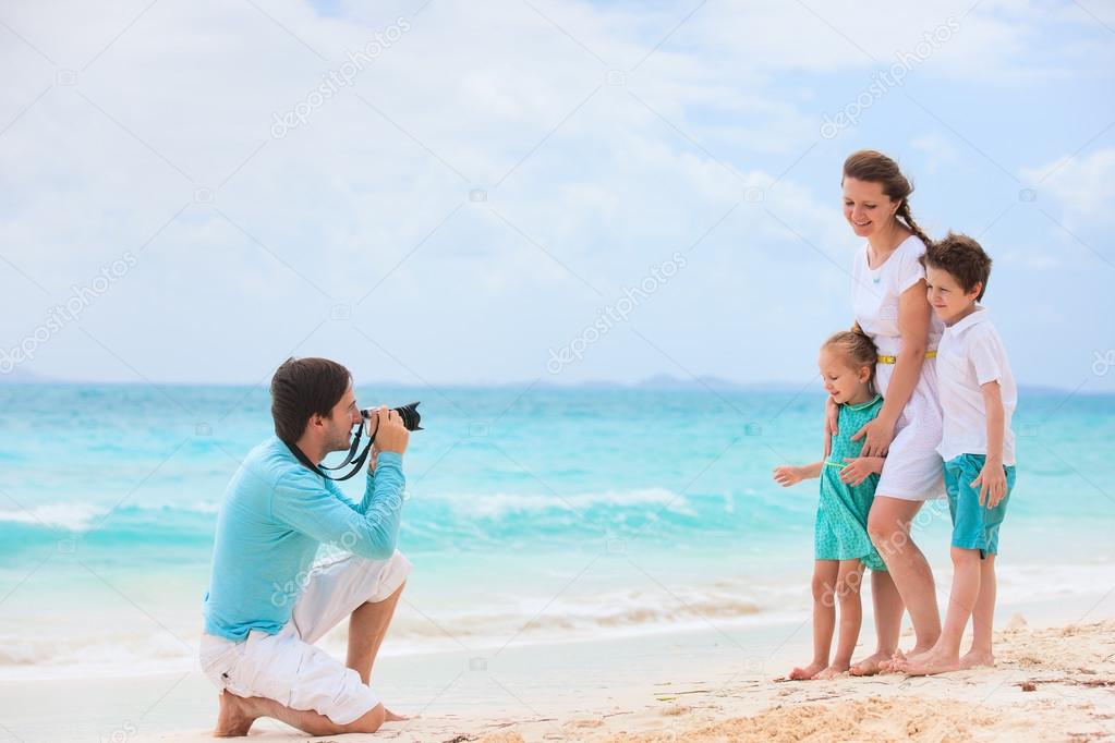 Young man making photo of his wife and kids at tropical beach