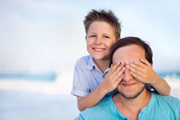 Хлопчик, що охоплюють батька очі на пляжі — стокове фото