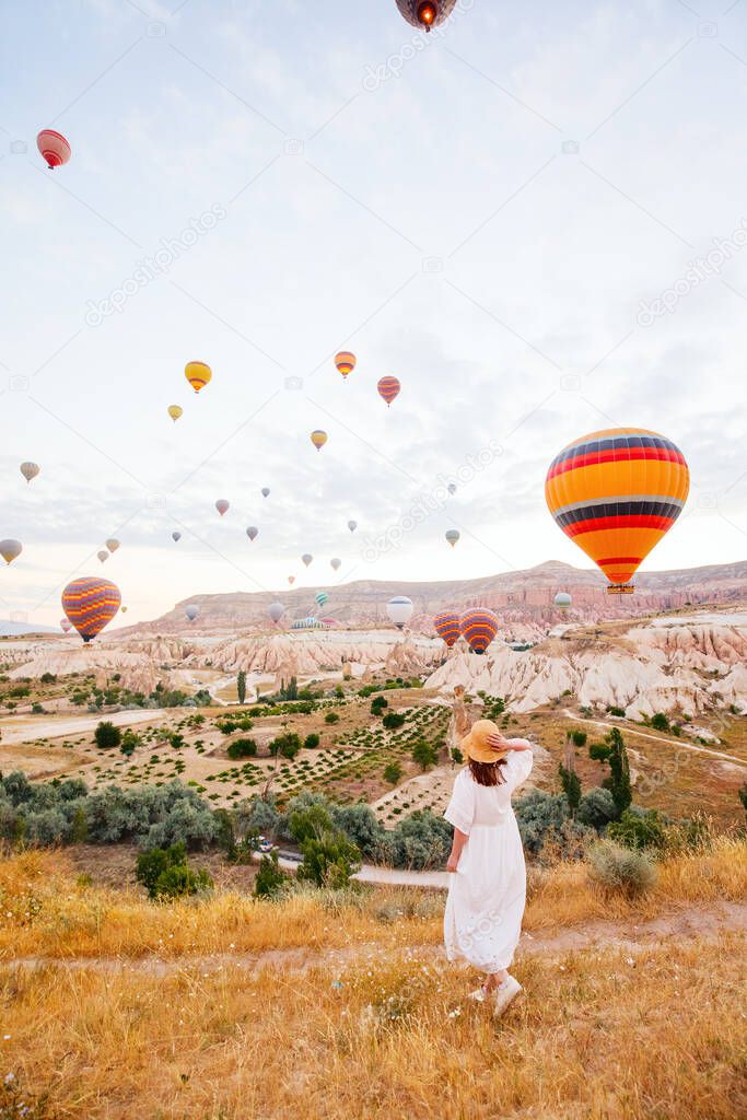 Back view of young woman admire scenery of hot air balloons flying over valley with rock formations and fairy chimneys in Cappadocia Turkey