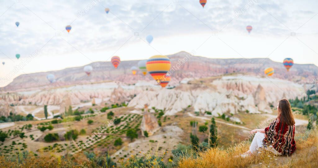Panoramic view of young woman admire scenery of hot air balloons flying over valley with rock formations and fairy chimneys in Cappadocia Turkey