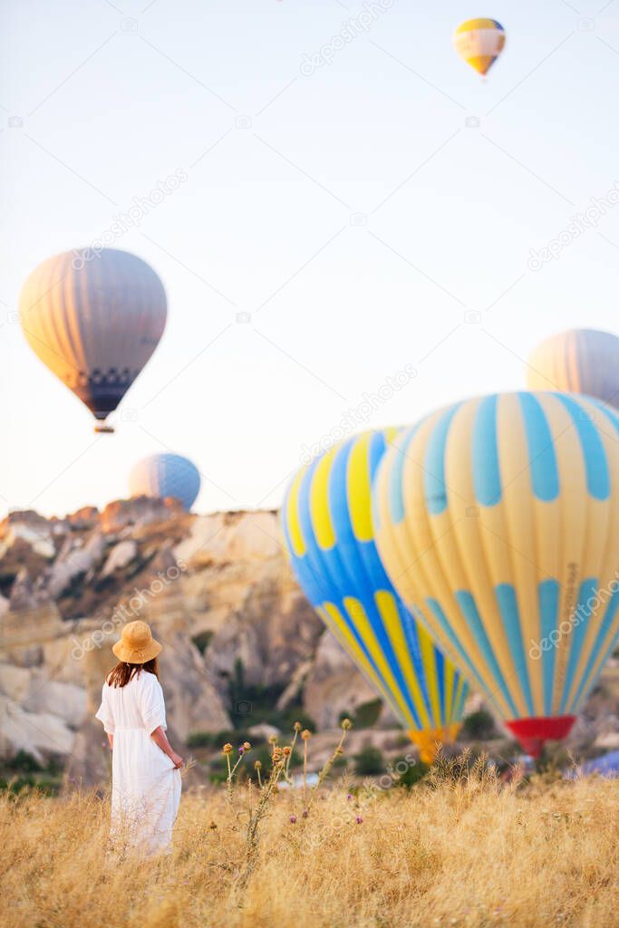 Back view of young woman admire scenery of hot air balloons flying over valley with rock formations and fairy chimneys in Cappadocia Turkey