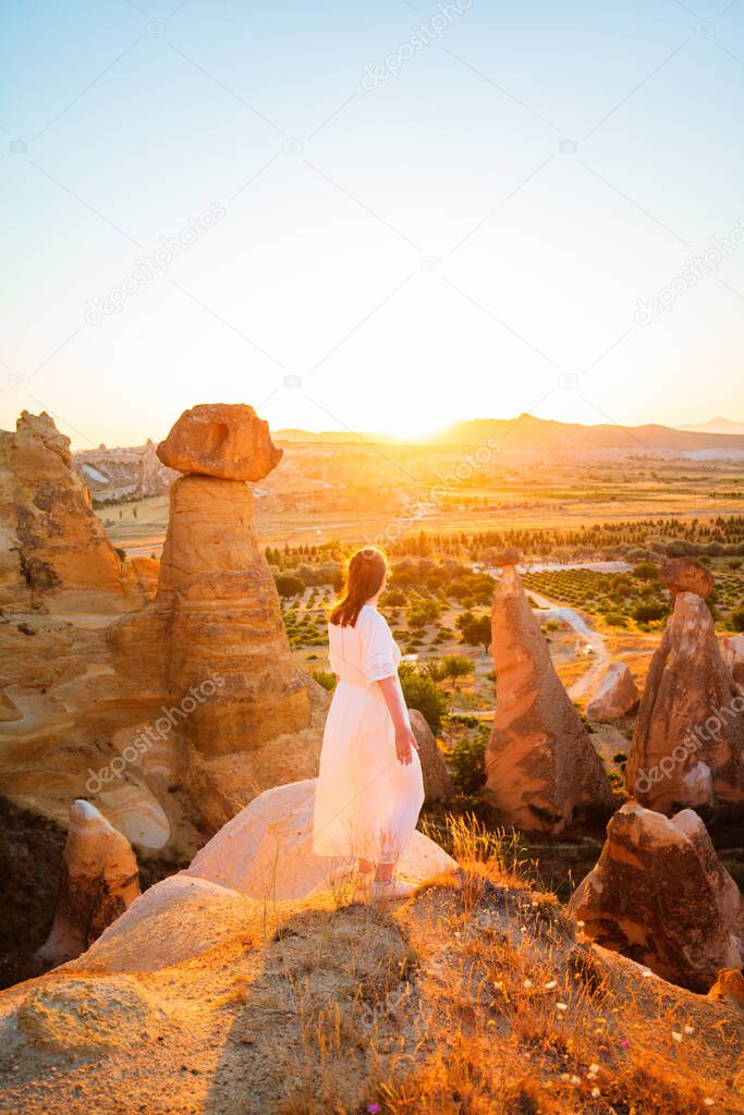 Back view of young woman enjoying stunning sunset while hiking around beautiful valley near Cavusin village in Cappadocia Turkey with amazing rock formations and fairy chimneys