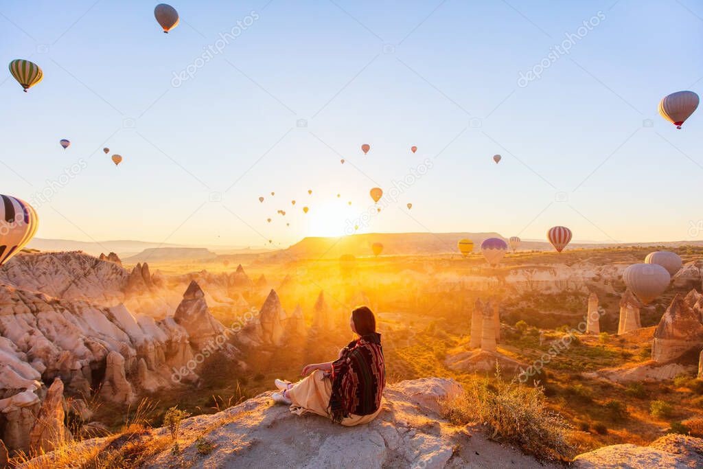 Young woman admire scenery of hot air balloons flying over Love valley with rock formations and fairy chimneys in Cappadocia Turkey