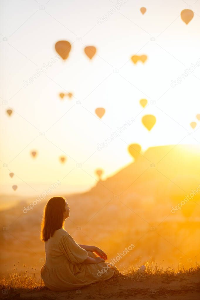 Young woman admire scenery of hot air balloons flying over Love valley with rock formations and fairy chimneys in Cappadocia Turkey