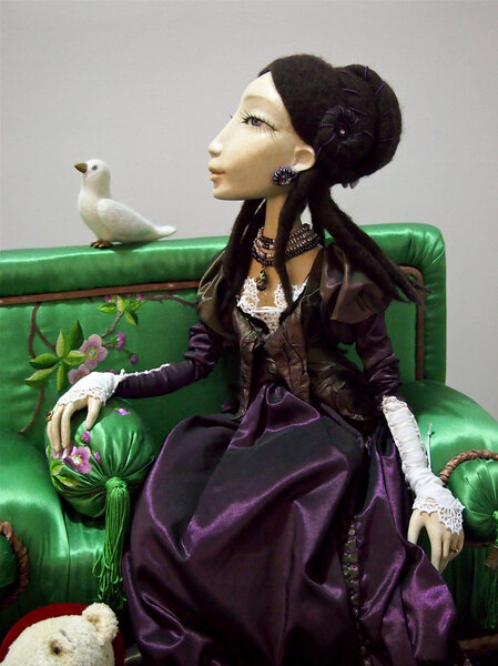 A collectible doll on green sofa with pigeon