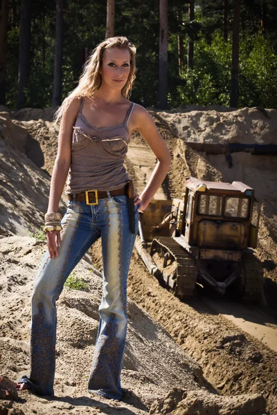 Cowgirl in jeans stands against the sand pit — Stock Photo, Image