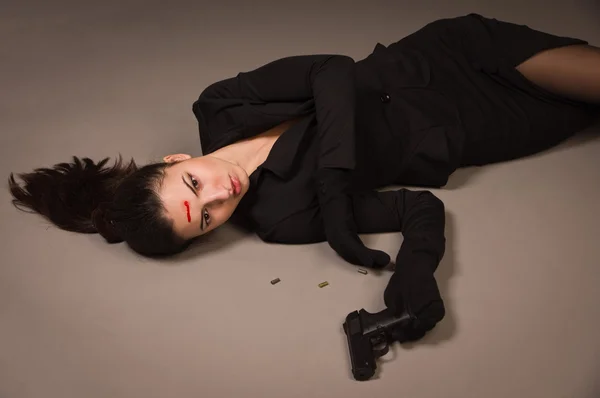 Žena v černém obleku s pistolí, ležící na podlaze — Stock fotografie