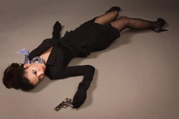 Kvinna i en svart kostym med pistol liggande på golvet — Stockfoto
