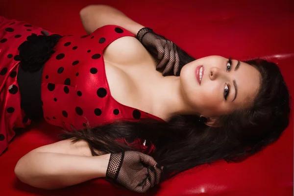 Pin-up girl lying on a red leather couch — Stock Photo, Image