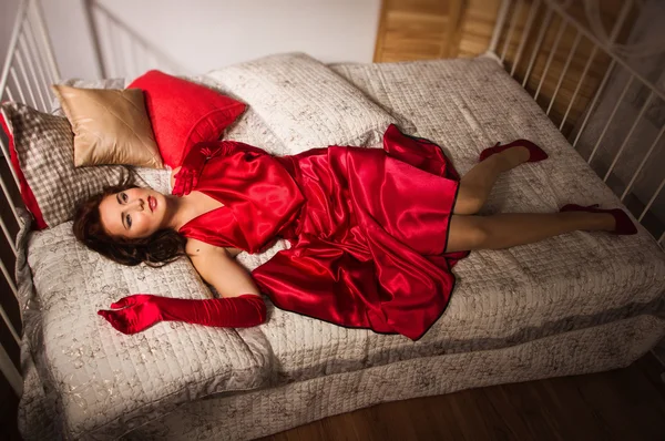 Sensuele brunette in een rode jurk liggend op het bed — Stockfoto