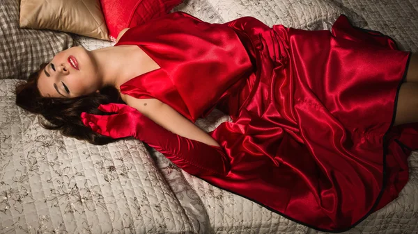 Sensuale bruna in un abito rosso sdraiato sul letto — Foto Stock