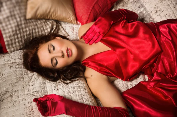 Sensuale bruna in un abito rosso sdraiato sul letto — Foto Stock