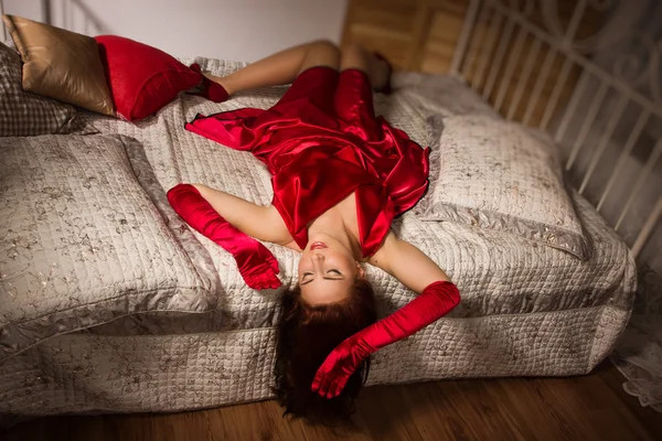 Morena sensual em um vestido vermelho deitado na cama — Fotografia de Stock