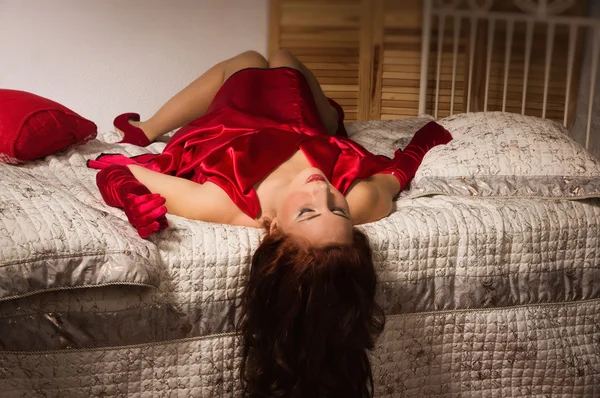 Sinnliche Brünette in einem roten Kleid auf dem Bett liegend — Stockfoto